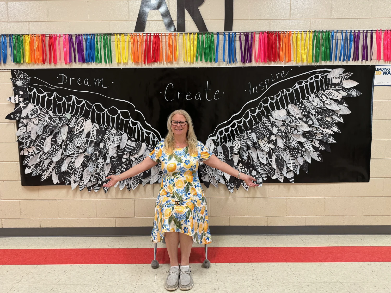 Beth standing before the collaborative black-and-white wings mural made by her third-grade students